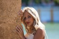 Portrait of a young, beautiful blonde woman leaning her hands on a brown wall with a shy look and bright eyes. The woman is Royalty Free Stock Photo