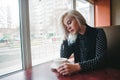 Portrait of a young beautiful blonde woman sitting in a cozy cafe near the window with a cup of coffee. Coffee Break Royalty Free Stock Photo