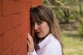 Portrait of young, beautiful, blonde woman in white shirt with her face leaning against a red brick wall, with flirtatious look. Royalty Free Stock Photo