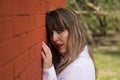 Portrait of young, beautiful, blonde woman in white shirt with her face leaning against a red brick wall, with flirtatious look. Royalty Free Stock Photo