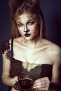 Portrait of young beautiful blue-eyed model with artistic leopard make-up holding a cup of coffee with beans on the saucer.