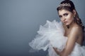 Portrait of young beautiful bride in diadem with naked shoulders clasping fluffy skirt of her wedding dress to her breast