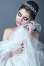 Portrait of young beautiful bride in diadem with naked shoulders touching fluffy skirt of her wedding dress with her cheek