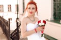 Portrait of a young beautiful bride in red sneakers with bouquet of roses on the city street. Royalty Free Stock Photo