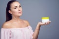 Portrait of young beautiful brunette with ponytail holding cosmetic jar on her palm and smiling. Royalty Free Stock Photo