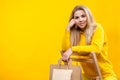 Portrait of young beautiful caucasian blonde woman with paper eco bags in yellow sportive suit, sitting on a wooden chair, Royalty Free Stock Photo