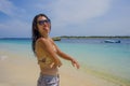 Young beautiful Chinese Asian girl in bikini having fun mocking with tongue out on beach with amazing beautiful turquoise sea wate