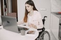 Young disabled woman in wheelchair working with laptop and tablet at home Royalty Free Stock Photo