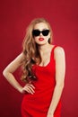 Portrait of young beautiful fashion woman wearing red dress and black sunglasses. model girl with red lips makeup on red