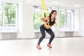 Portrait of young beautiful fit woman in black sportswear training arms with trx fitness straps in the gym doing push ups train Royalty Free Stock Photo