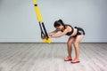 Portrait of young beautiful fit woman in sportswear doing a squat exercise with fitness straps in the gym. TRX functional training Royalty Free Stock Photo