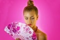 Portrait of a young beautiful girl with bright make-up and colored fan in hands close-up on the pink background. Geisha Royalty Free Stock Photo