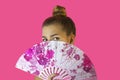 Portrait of a young beautiful girl with bright make-up and a fan in hands close-up on a pink background. Royalty Free Stock Photo