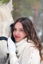 Portrait of a young, beautiful girl in close-up with a white horse in winter