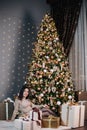 portrait of a young, beautiful girl in a dress near the Christmas tree with a bunch of gifts