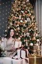 portrait of a young, beautiful girl in a dress near the Christmas tree with a bunch of gifts