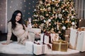 portrait of a young, beautiful girl in a dress near the Christmas tree with a bunch of gifts