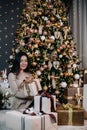 portrait of a young, beautiful girl in a dress near the Christmas tree with a bunch of gifts