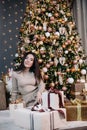 portrait of a young, beautiful girl in a dress near the Christmas tree with a bunch of gifts