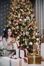 portrait of a young, beautiful girl in a dress near the Christmas tree with a bunch of gifts