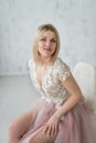 Portrait of a young beautiful girl in an evening dress with lace and pink fartine on the background of a white textural wall.