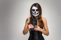 Portrait of young beautiful girl with fearful halloween skeleton makeup holding Holy Bible over gray background