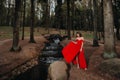 Portrait of a young beautiful girl with long brown hair, in a long red dress, the time of year. A girl walks along a stream in the