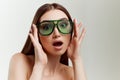 Portrait of young beautiful girl with nude make up, in green sunglasses posing with shocked face over grey studio Royalty Free Stock Photo