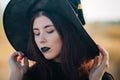 Portrait of a beautiful girl with pale skin and black lips in a big black hat. Woman in the image of a witch for Halloween. Royalty Free Stock Photo