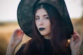 Portrait of a beautiful girl with pale skin and black lips in a big black hat. Woman in the image of a witch for Halloween. Royalty Free Stock Photo