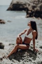 Portrait of young beautiful tanned girl in white bikini sitting at rocks near blue green clear ocean sea water. Sunbathing wo Royalty Free Stock Photo