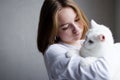 Portrait of a young beautiful girl in a white sweater on a white background with a cute white cat in her arms. Kitten enjoys being