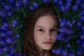 Portrait of young beautiful girl woman with brown hair lying on grass with blue flowers around her head. Close up, top Royalty Free Stock Photo