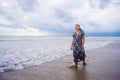 Portrait of young beautiful and happy Asian Chinese woman on her 20s or 30s wearing long chic dress walking alone on beach sea