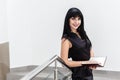 Portrait of Young Beautiful happy brunette woman dressed in a black business suit working with a notebook, standing in a office, Royalty Free Stock Photo