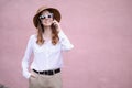 Portrait of a beautiful happy business woman in sunglasses,a hat outdoors talking on the phone on a pink background Royalty Free Stock Photo