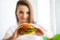 Portrait of young beautiful hungry woman eating burger.