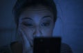 Portrait of young beautiful latin woman using mobile phone late night sleepless lying in bed in the dark in smartphone and interne Royalty Free Stock Photo