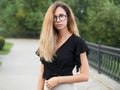 Portrait of young beautiful long hair woman wearing black blouse, holding mobile phone at summer green park path background. Royalty Free Stock Photo