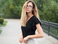 Portrait of young beautiful long hair woman wearing black blouse, holding mobile phone at summer green park path background. Royalty Free Stock Photo