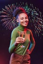 Portrait of a young beautiful mixed race woman holding glass of champagne and smiling at camera, standing against Royalty Free Stock Photo