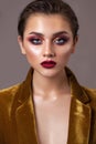 Portrait of a young beautiful model with evening make-up, red smoky eyes and lips and hair pulled back in a ponytail.