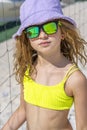 Portrait of a young beautiful model girl with hat and sunglasses posing on the beach. Wearing a bright yellow bikini swimsuit. Royalty Free Stock Photo