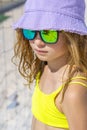 Portrait of a young beautiful model girl with hat and sunglasses posing on the beach. Wearing a bright yellow bikini Royalty Free Stock Photo