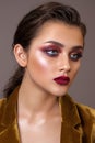 Portrait of a young beautiful model with evening make-up, red smoky eyes and lips and hair pulled back in a ponytail.