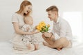 Portrait of young beautiful mother sitting, kneeling, holding little plump baby and handsome father presenting bouquet. Royalty Free Stock Photo