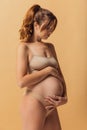 Portrait of young beautiful pregnant woman in lingerie isolated over sand color studio background. Natural beauty, happy Royalty Free Stock Photo