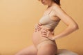 Portrait of young beautiful pregnant woman in lingerie isolated over sand color studio background. Natural beauty, happy Royalty Free Stock Photo