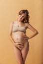 Portrait of young beautiful pregnant woman in lingerie isolated over sand color studio background. Natural beauty, happy Royalty Free Stock Photo