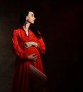 Portrait of young beautiful pregnant woman in red elegant maxi dress standing, embracing belly and looking aside Royalty Free Stock Photo